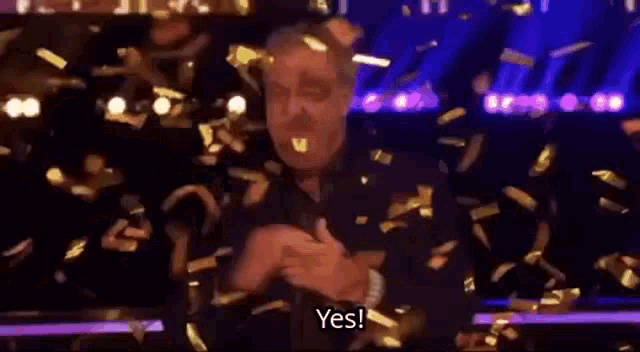 a man is standing in front of a crowd with confetti falling around him and says yes .