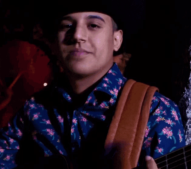 a man wearing a cowboy hat and a floral shirt holds a guitar