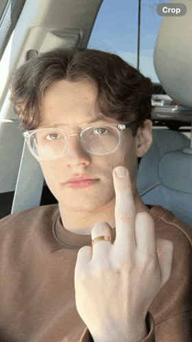 a young man wearing glasses and a ring is giving the middle finger in a car