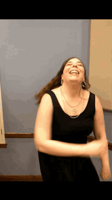 a woman in a black tank top is laughing and dancing