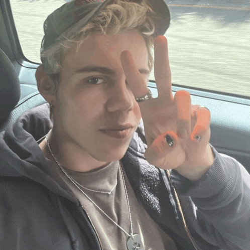 a young man wearing a hat and a necklace gives a peace sign