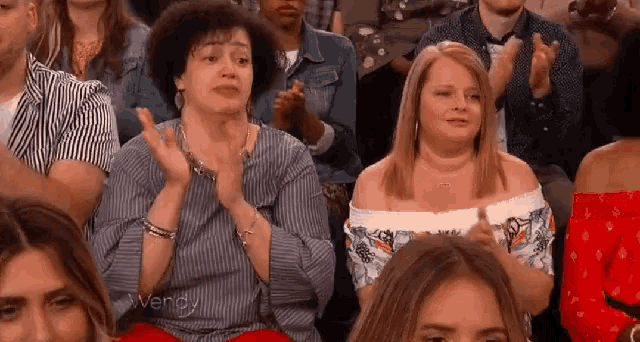 a group of people are sitting in a row clapping their hands in a crowd .