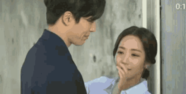 a man and a woman are standing next to each other and the woman is covering her mouth .