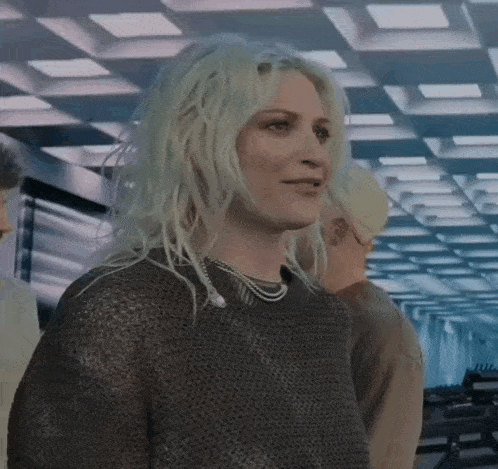 a woman with blonde hair is wearing a sweater and a necklace while standing in a room .