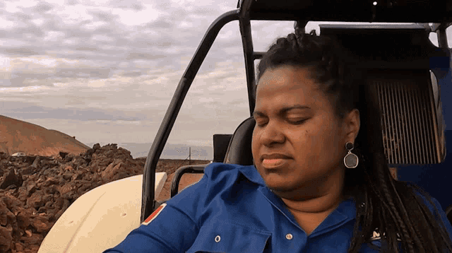 a woman in a blue shirt is sitting in a car with her eyes closed