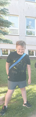 a boy wearing a black shirt and grey shorts is standing in the grass