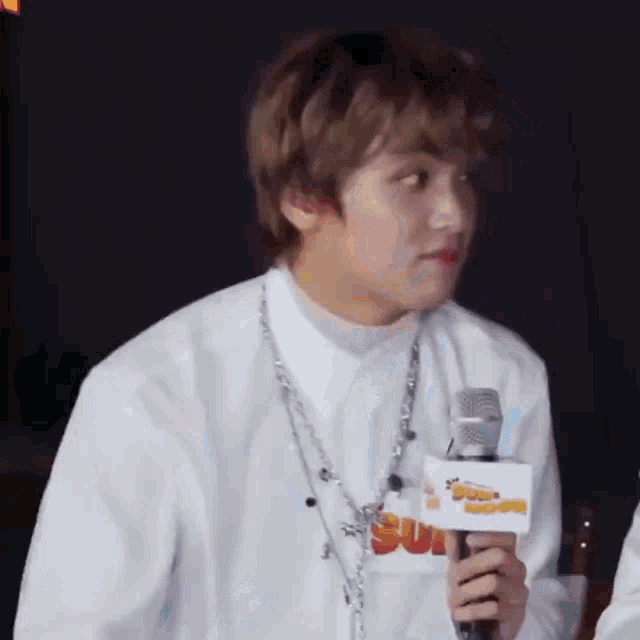 a man in a white shirt is holding a microphone and talking into it .