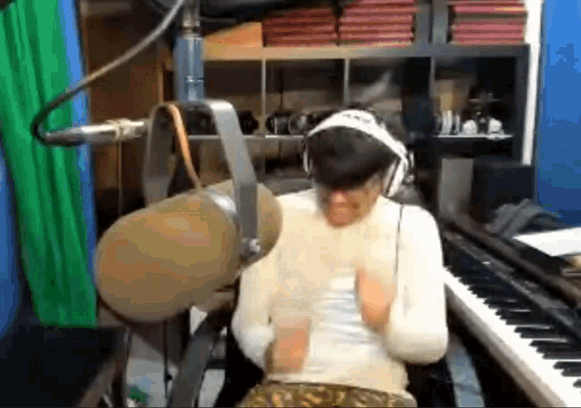 a man wearing headphones and a headband is sitting in front of a microphone and a piano .