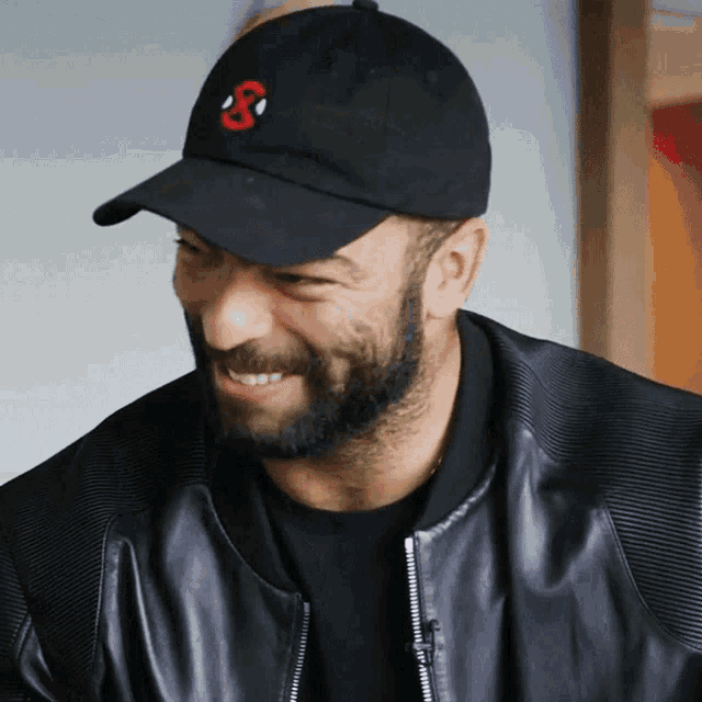 a man with a beard wearing a black hat with a red s on it