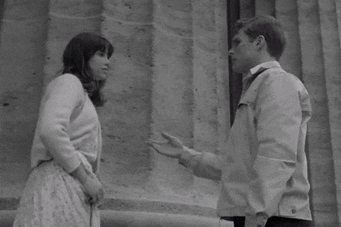 a man and a woman are standing next to each other and talking in front of a building .