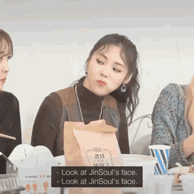 a woman sitting at a table with a bag that says jin soul 's face on it