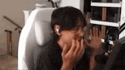 a man is sitting in a chair wearing headphones and covering his mouth with his hands .