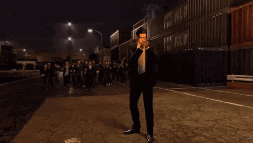 a man in a suit smoking a cigarette stands in front of a crowd of people