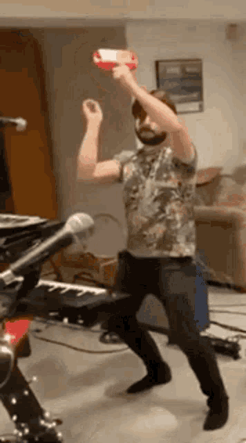 a man in a floral shirt is dancing in a living room while holding a red object over his head .