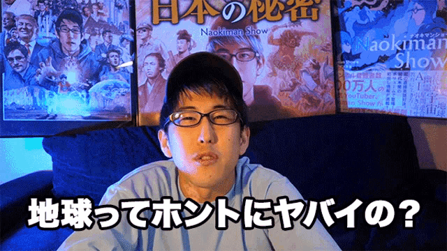 a man wearing glasses sits on a couch in front of a poster for naokimen show