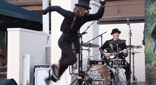 a man in a top hat jumps in the air in front of a drum set that says giraffe on it
