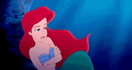 ariel from the little mermaid is sitting in the ocean with her arms crossed and her hair blowing in the wind .