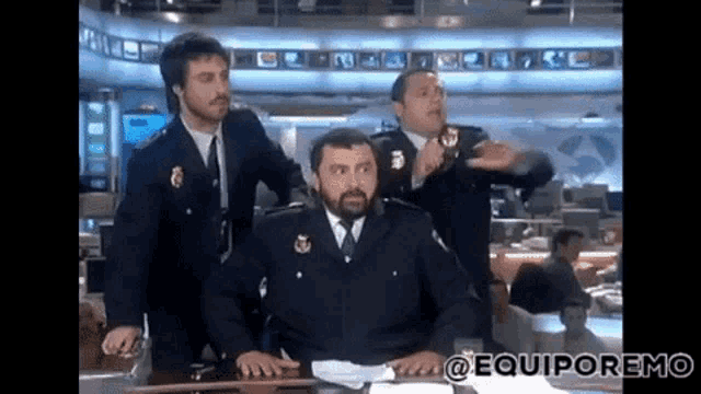 a man in a police uniform is sitting at a desk in front of two other men ..