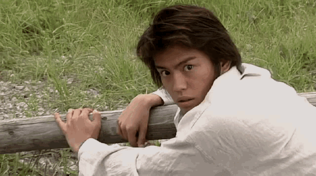 a young man is leaning on a wooden fence post .
