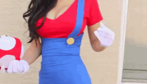a woman in a mario costume is holding a mushroom and giving a peace sign .
