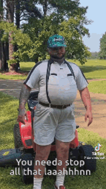 a man is standing next to a lawn mower wearing suspenders .