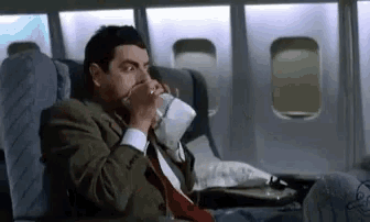 a man in a suit and tie is drinking coffee on an airplane .