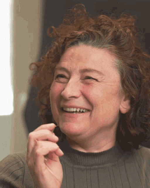 a woman with curly hair is smiling and holding her hand to her face