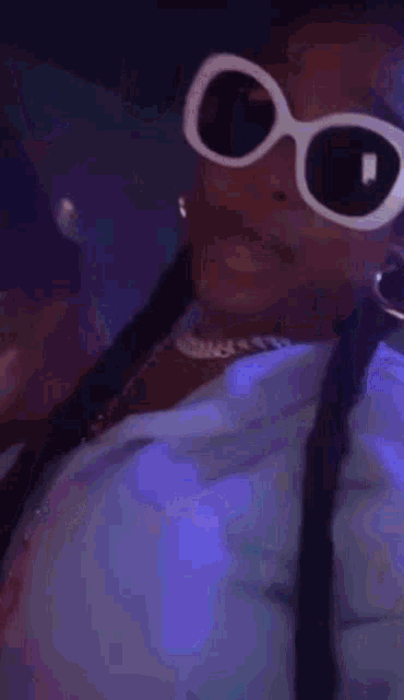 a woman wearing sunglasses and a necklace is standing in front of a blue background .
