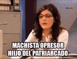 a woman wearing glasses is sitting at a desk with the words machista opresor hijo del patriarcado above her