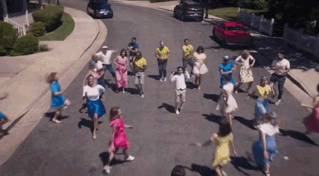 a group of people dancing on a street with a red car behind them