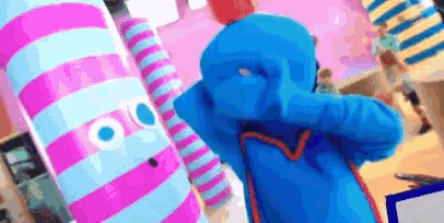 a person in a blue costume stands next to a pink and white striped object
