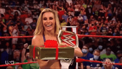 a woman in a wrestling ring holding a gift box and a wrestling championship .