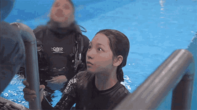 a woman in a wet suit is standing in a swimming pool with a man in a wet suit behind her