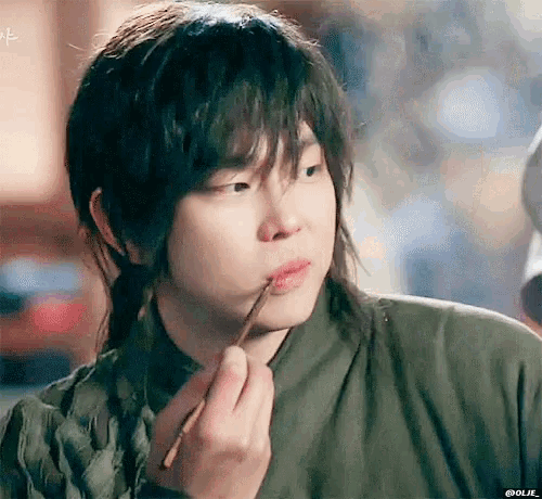 a young man is applying lip gloss with a brush .