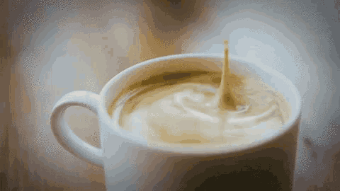 a drop of milk is falling into a cup of coffee .