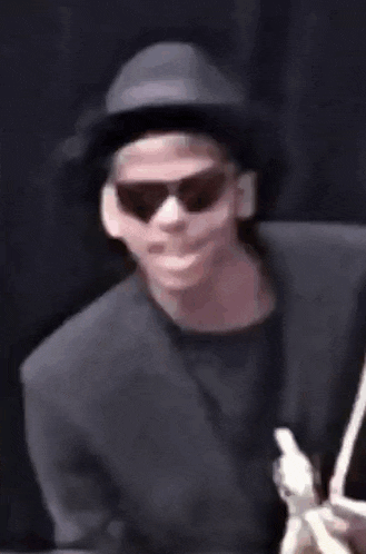 a man wearing a hat and sunglasses is smiling while holding a cell phone .