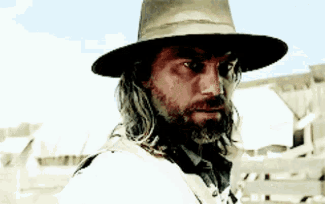 a man with long hair and a beard is wearing a hat and looking at the camera .
