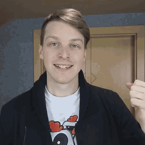 a man wearing a black jacket and a white shirt with hearts on it is smiling