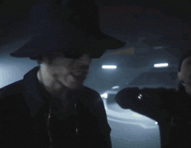 a man wearing a black hat and sunglasses stands in the dark