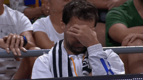 a man covering his face with his hand while sitting in a crowd