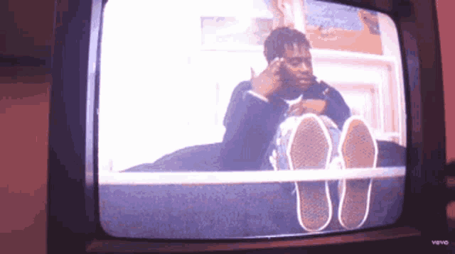 a man sitting on a bed with his feet up on a television screen