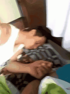 a man in a white tank top is laying on a bed with his head on a pillow .