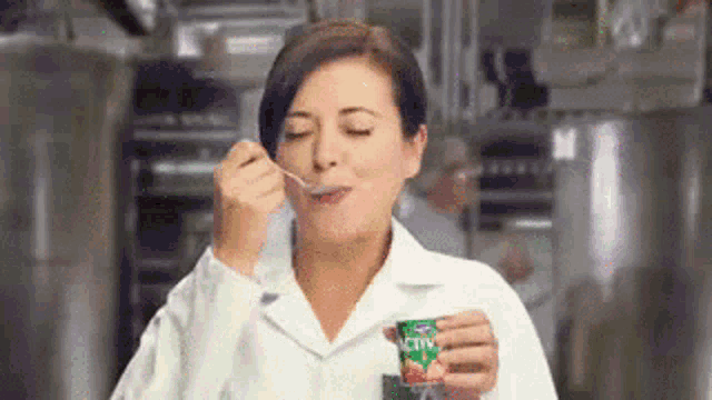 a woman in a lab coat is eating yogurt from a carton