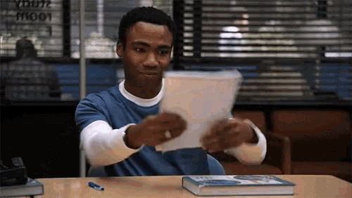 a man is sitting at a desk holding a piece of paper in front of a book .