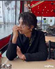 a woman is sitting at a table in a restaurant looking out the window .