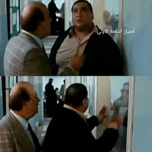 two bald men are standing next to each other in a hallway with arabic writing on the bottom right