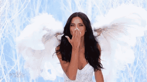 a woman with angel wings is blowing a kiss while wearing a white dress .