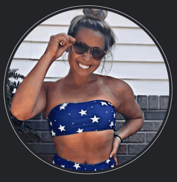 a woman in a blue and white bikini top and sunglasses is smiling and standing in front of a brick wall .