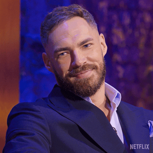 a man with a beard is wearing a suit and smiling in front of a netflix logo .