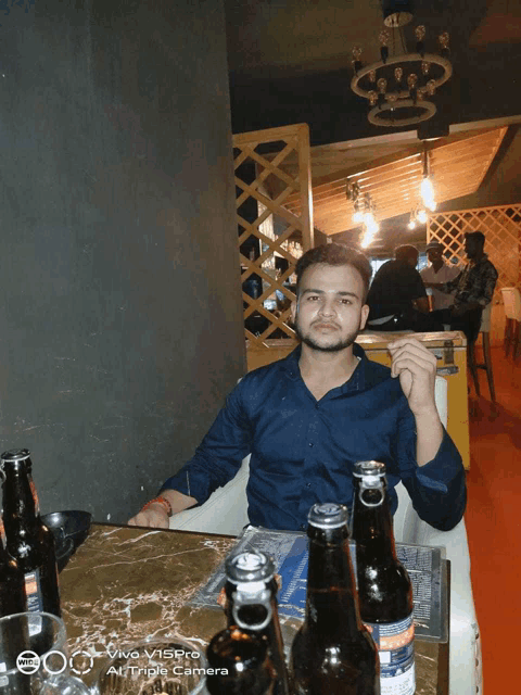 a man sits at a table with bottles of beer and a vivo v5pro camera